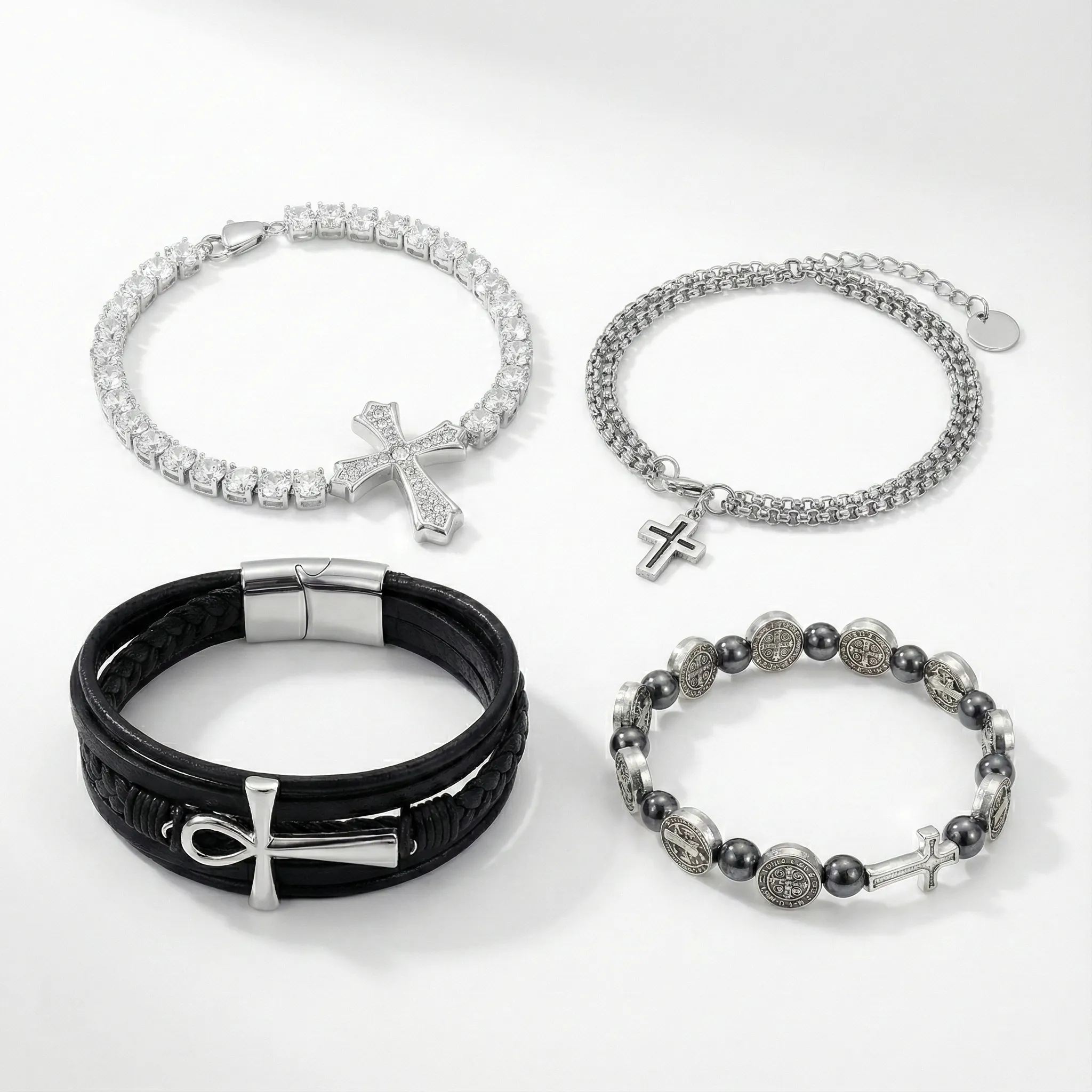 Diverse collection of cross bracelets: Sparkly crystal tennis cross bracelet, layered silver chain, black leather Ankh cross wristband, and Catholic Saint Benedict bead bracelet.