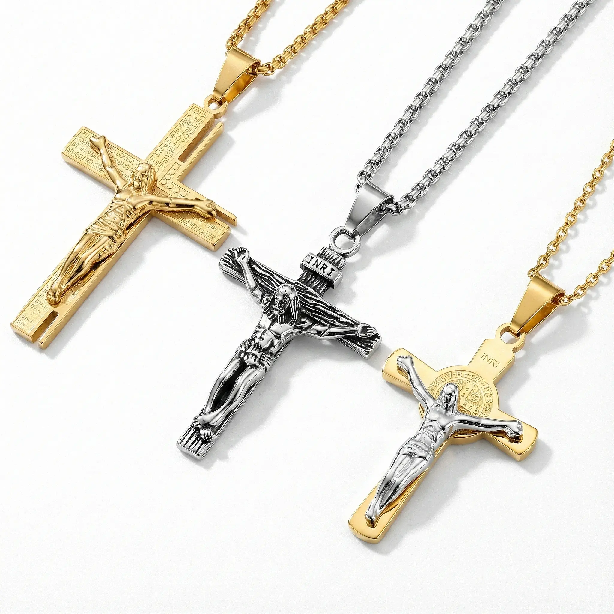 Trio of stainless steel crucifix necklaces: Gold scripture-engraved cross, silver antique finish INRI pendant, and two-tone St. Benedict crucifix on durable box chains.