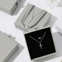 Silver cross necklace and matching ring displayed inside a premium grey drawer-style jewelry box with black velvet lining.