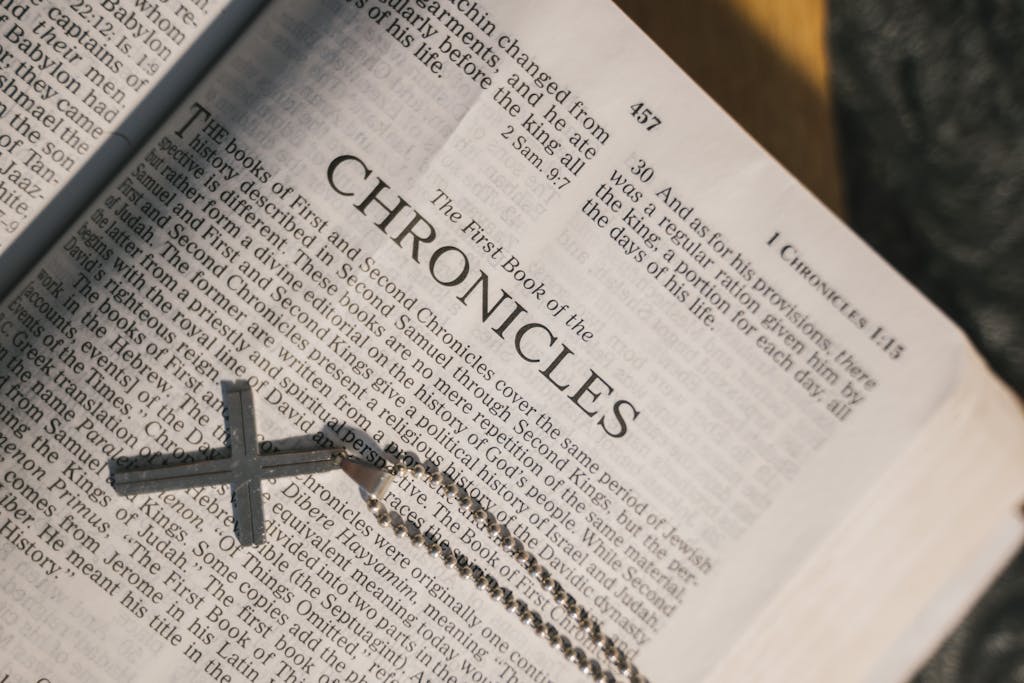 An open Bible displaying Chronicles with a cross pendant laying on its pages, symbolizing faith and scripture.
