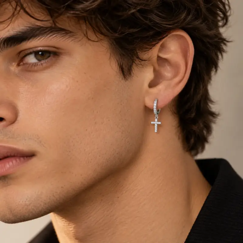diamond cross earrings for men varro Man with wavy dark hair wearing a silver pavé cross earring, close-up side view