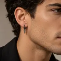 Black cross hoop earring worn by a dark-haired man in a black jacket, side profile