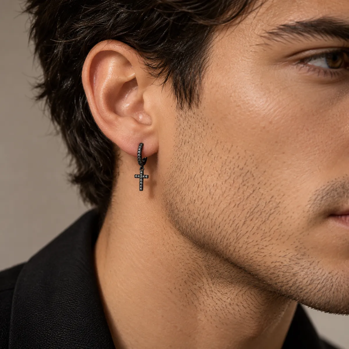 Black cross hoop earring worn by a dark-haired man in a black jacket, side profile