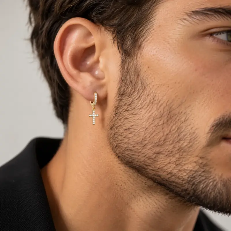 diamond cross earrings dangle mens varro Man wearing one gold pavé cross hoop earring, close-up with beard and dark jacket
