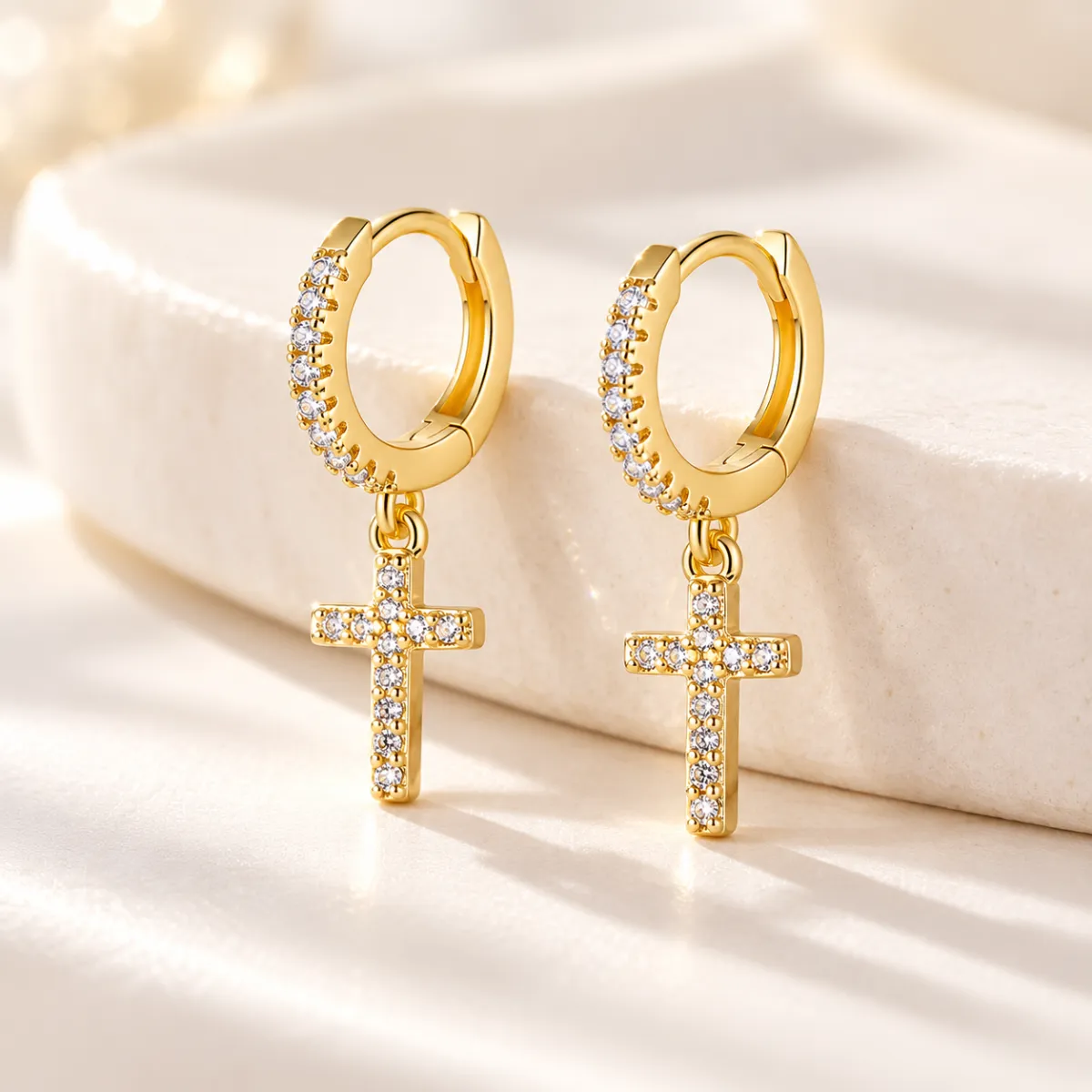 Men’s CZ cross hoop earrings in 14k gold plating resting on a cream stone ledge