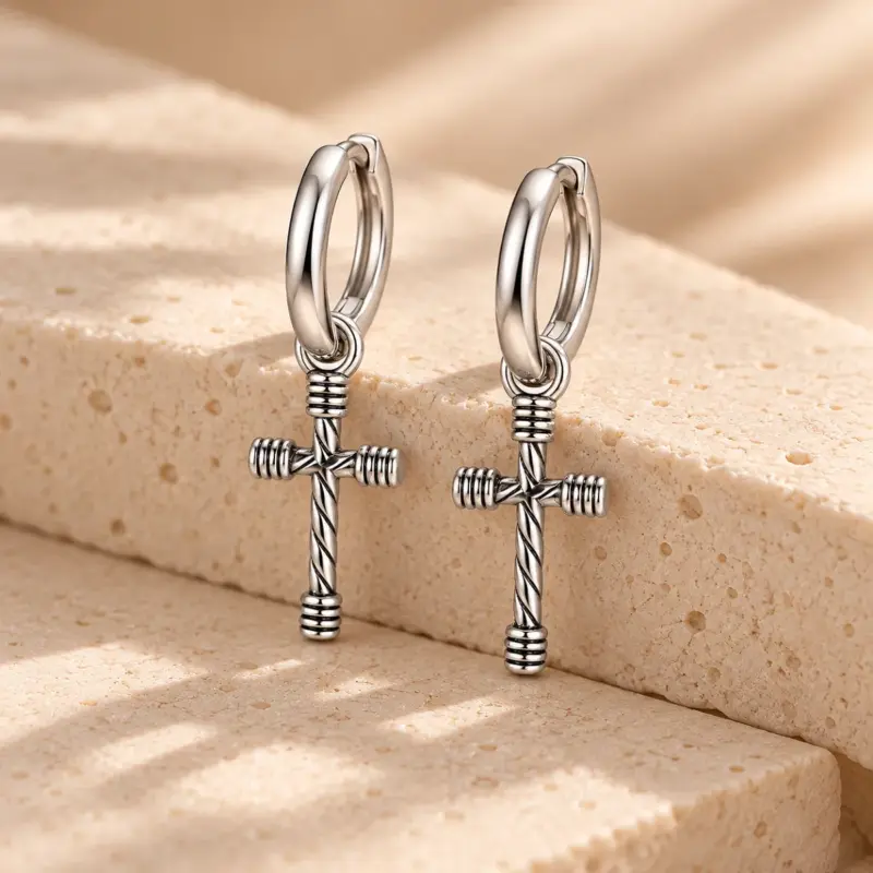 cross earrings men style Menâs stainless steel cross earrings with wrapped ends resting on a sandy stone block