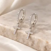 Diamond-look cross earrings for men in silver tone, propped on a beige marble ledge
