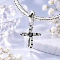 Black stone cross charm hanging from a silver snake chain bracelet, soft blue background