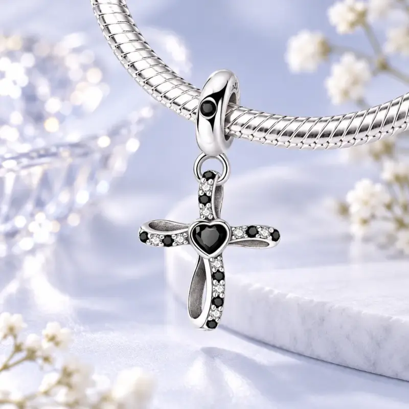 black-cross-charm-on-bracelet Black stone cross charm hanging from a silver snake chain bracelet, soft blue background