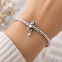 Praying hands cross charm worn on a woman's wrist with silver snake chain bracelet