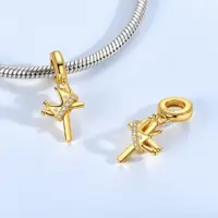 Gold cross charm with crown hanging from a silver snake chain bracelet, pale blue backdrop