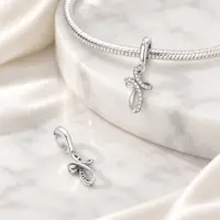 Silver CZ cross charm on snake chain bracelet beside a second charm showing its open back