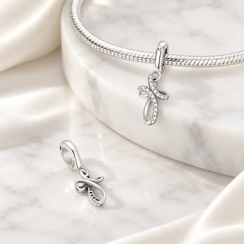 diamond cross charm perpetua Silver CZ cross charm on snake chain bracelet beside a second charm showing its open back