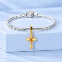14k gold cross dangle on a silver snake chain bracelet with heart clasp, blue backdrop