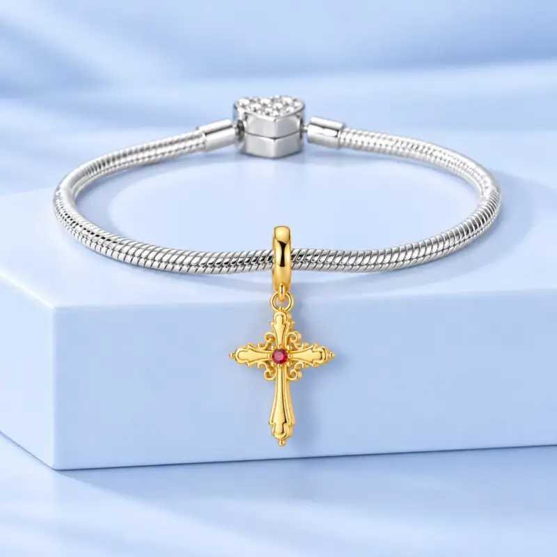 gold plated cross charmâ 14k gold cross dangle on a silver snake chain bracelet with heart clasp, blue backdrop