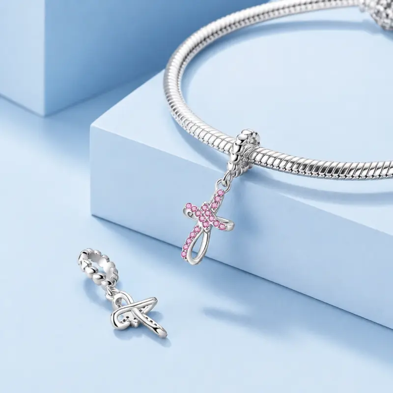pink-silver-cross-charm-pair Pink and plain silver cross charms beside a snake chain bracelet on blue blocks