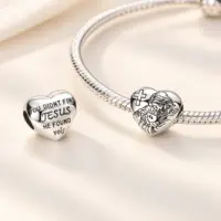 Silver Jesus heart charm on a snake chain bracelet beside its verse side, cream satin
