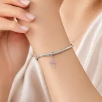 Woman wearing a pink stone cross charm on a silver snake chain bracelet