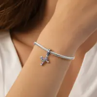 Silver cross and crown charm with pink stones worn on a woman’s wrist on a snake chain charm bracelet.