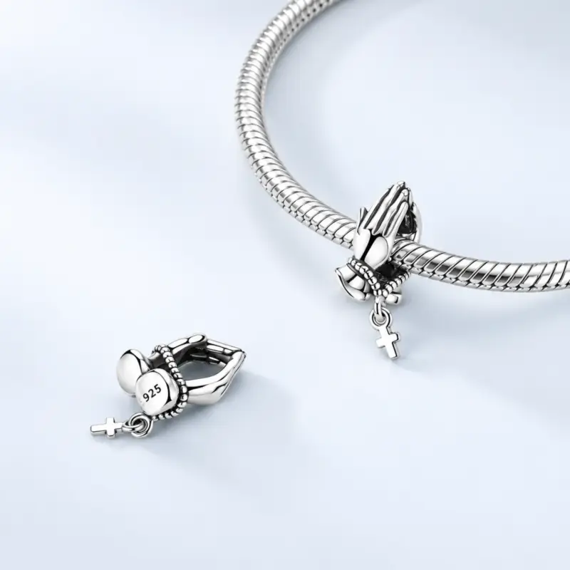 hand-cross-charm-snake-bracelet Silver hand cross charm threaded on snake chain bracelet beside a second charm showing 925 stamp