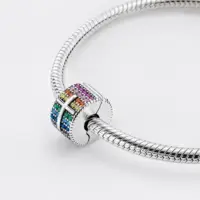 Woman wearing a rainbow pavé cross charm clipped to a silver snake chain bracelet