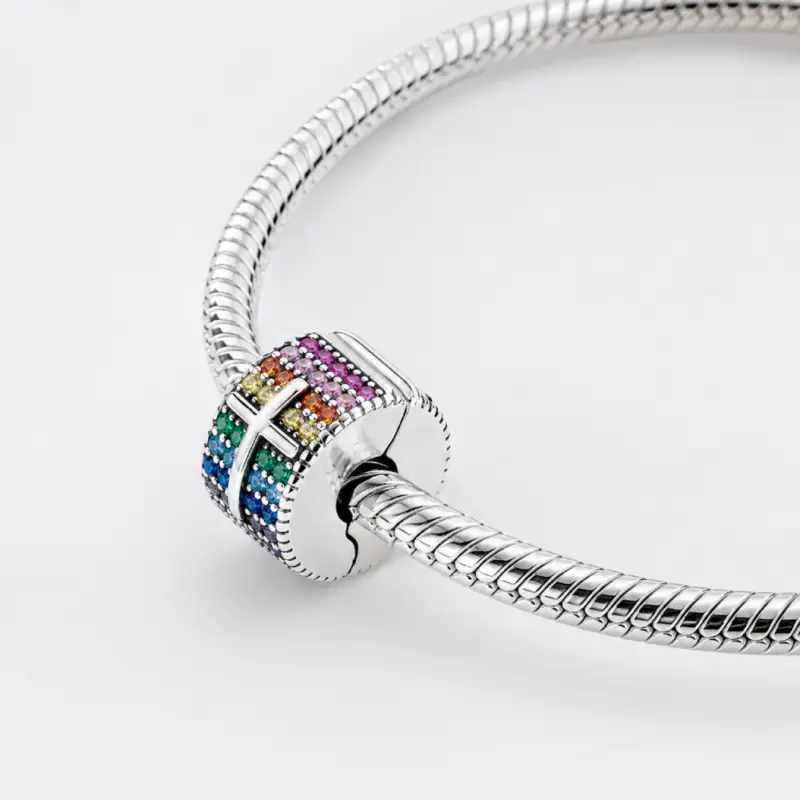 rainbow-cross-charm-worn-wrist Woman wearing a rainbow pavé cross charm clipped to a silver snake chain bracelet