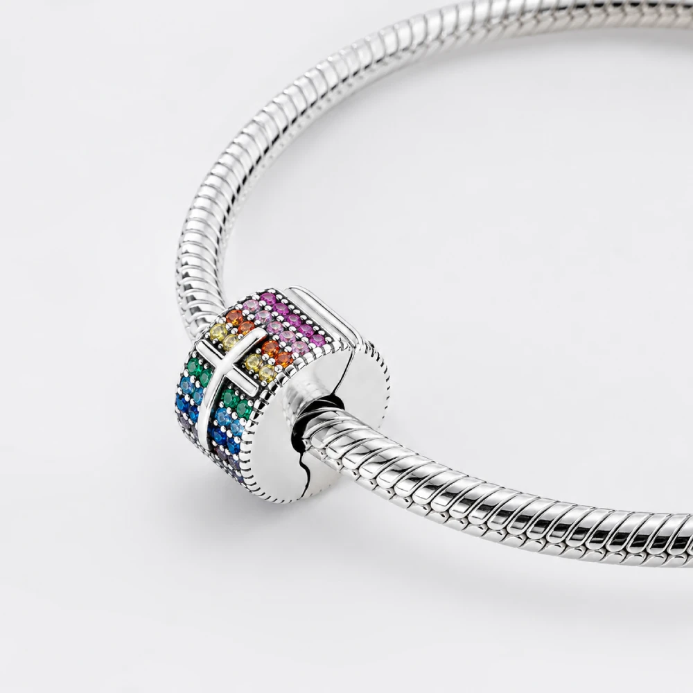 Woman wearing a rainbow pavé cross charm clipped to a silver snake chain bracelet