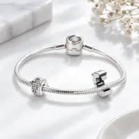 Small silver cross charm clipped to a snake chain bracelet beside an open clip