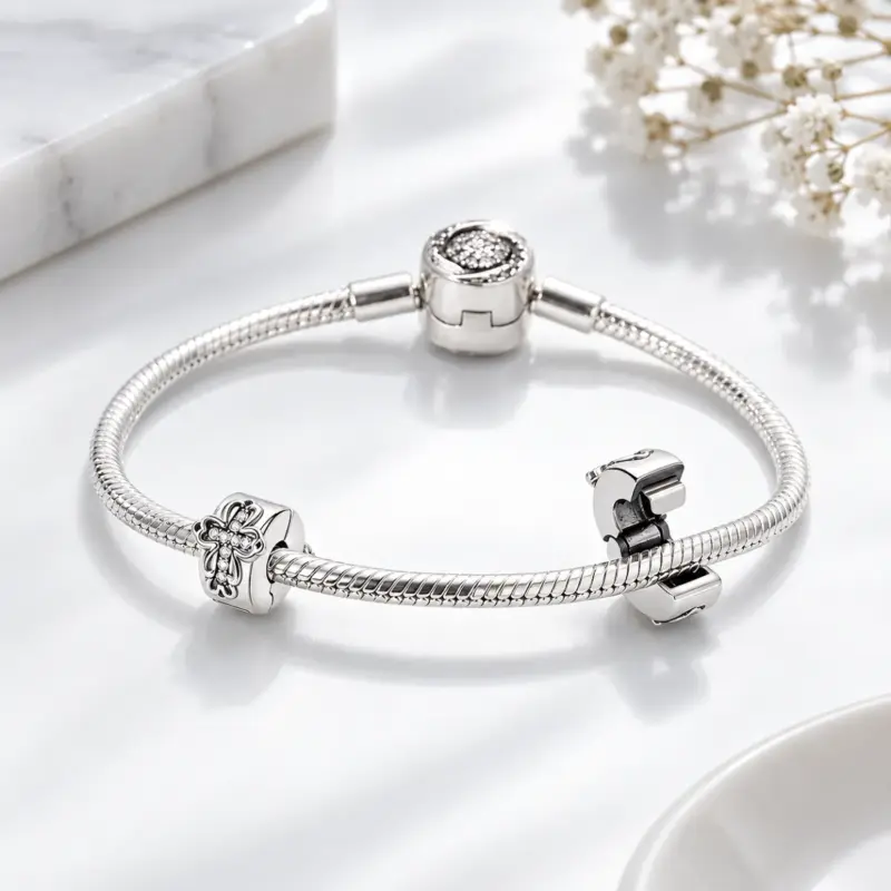 small-cross-charm-snake-bracelet Small silver cross charm clipped to a snake chain bracelet beside an open clip