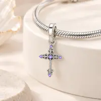 Purple stone cross dangle hanging from a silver snake chain bracelet on beige props