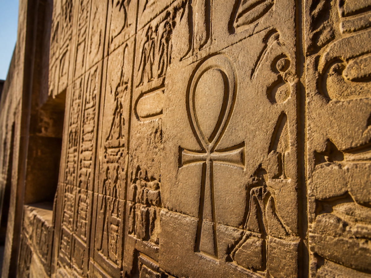 Ancient Egyptian hieroglyphs carved on a stone temple wall featuring the ankh symbol