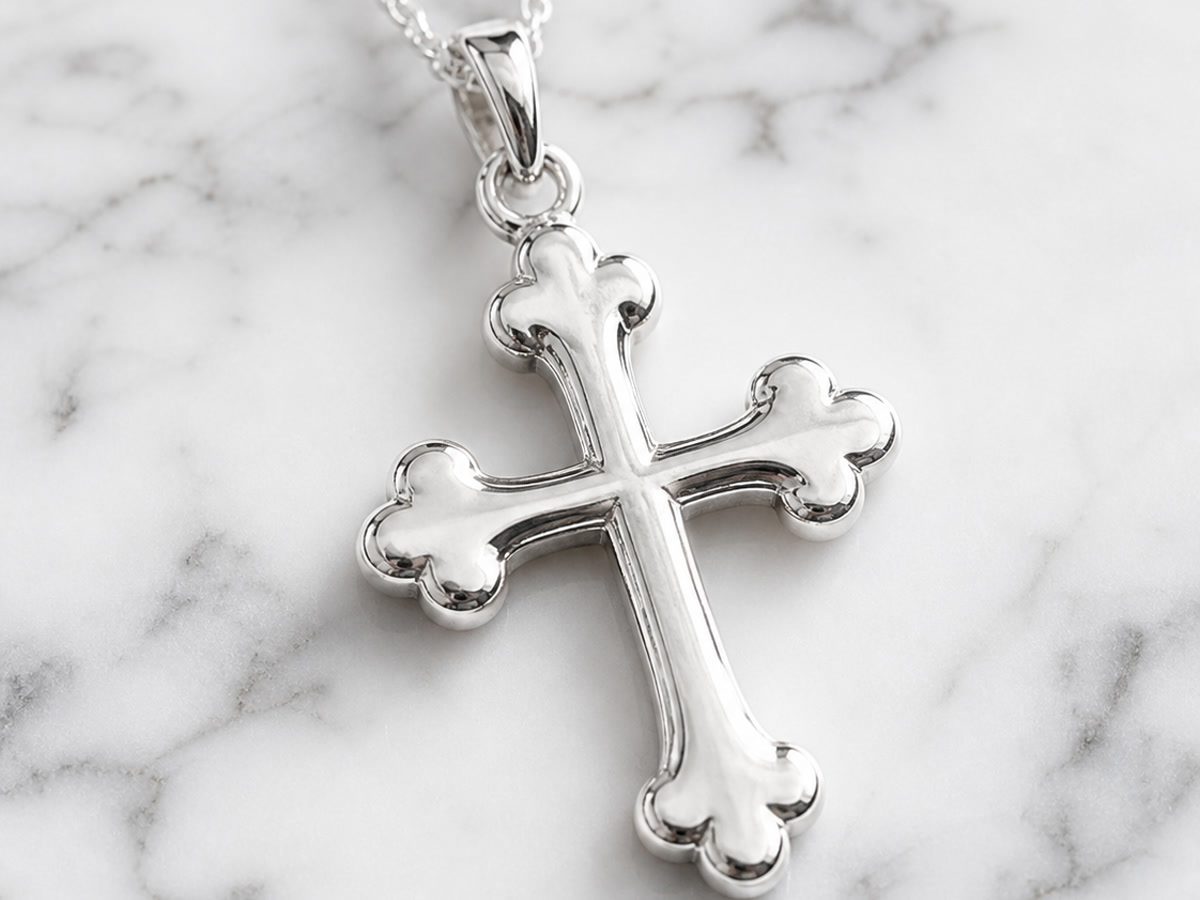 Sterling silver budded cross pendant with trefoil endings on each arm, hanging from a delicate chain on a white marble surface