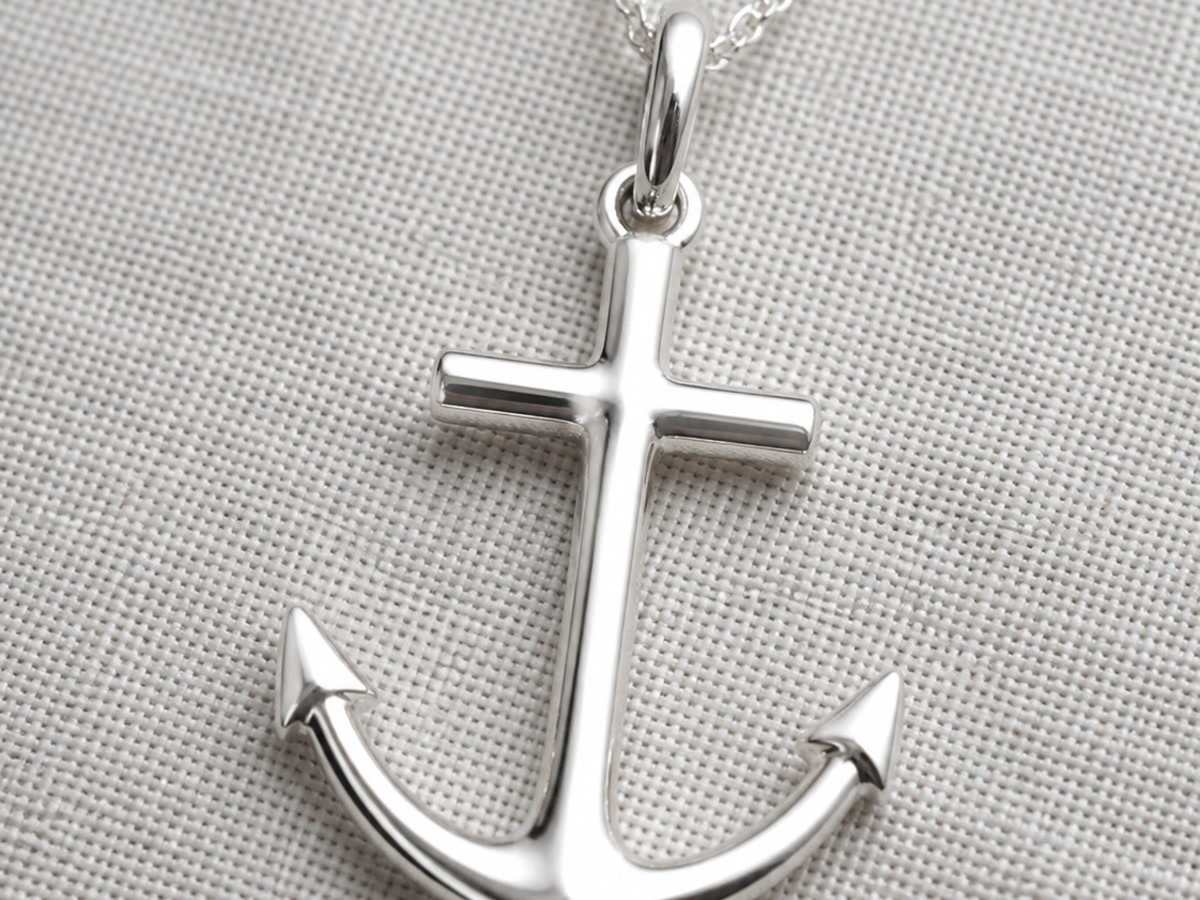 Sterling silver mariner cross pendant shaped like an anchor with curved arms, displayed on a light grey linen background