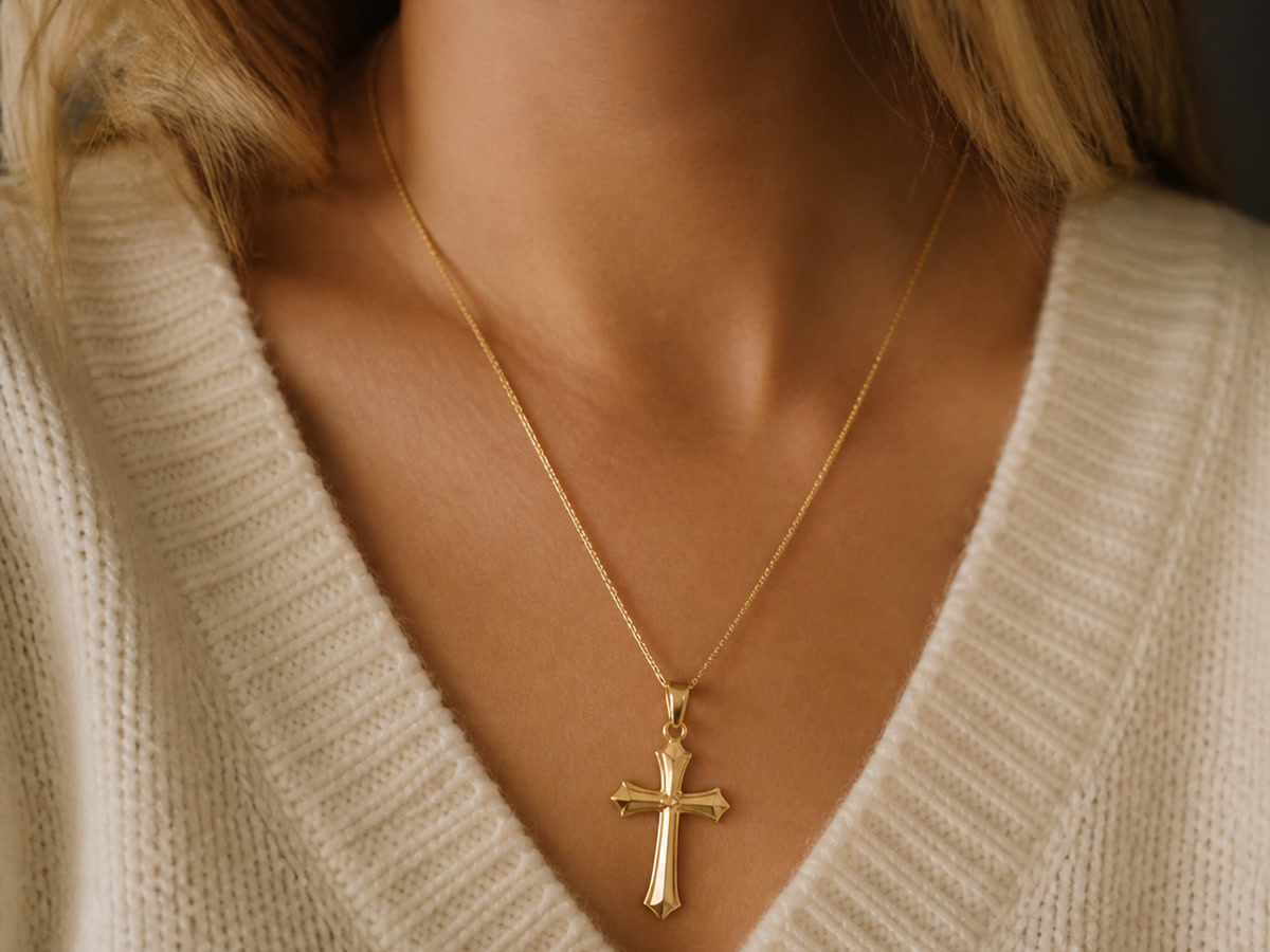 Woman wearing a bright gold-plated cross necklace against a cream sweater, showcasing the maintained shine