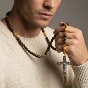Man holding a tiger eye beaded necklace with silver cross pendant
