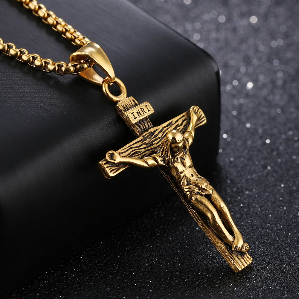 18k gold-plated crucifix necklace resting on a black block against a dark background