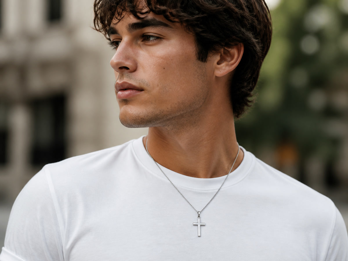 Person wearing a sleek stainless steel cross necklace against a white t-shirt, clean modern casual style.