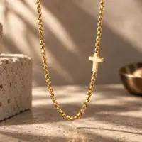 Gold cross station necklace draped over pale travertine stone in warm light