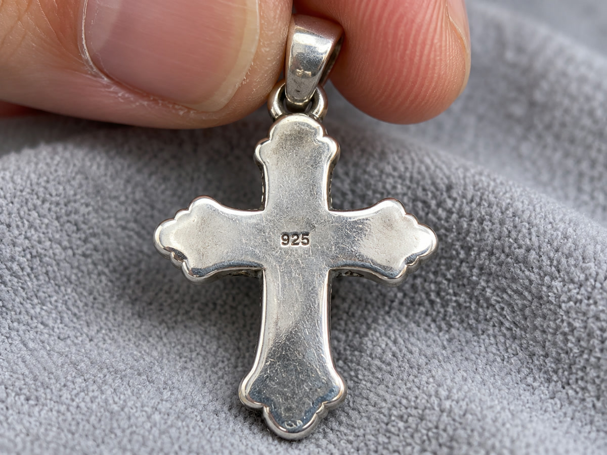Close-up of a 925 hallmark stamped on the back of a sterling silver cross held over a soft jeweler's cloth
